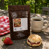 Thumbnail for Java Momma Strawberry Shortcake Coffee bag on a picnic table with a ceramic mug and a strawberry shortcake biscuit