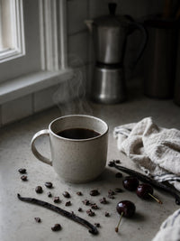 Thumbnail for Steaming coffee mug on a kitchen counter with cherries and vanilla beans.