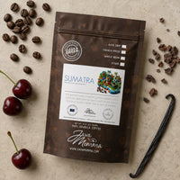 Thumbnail for Overhead flatlay of Java Momma Sumatra Medium Roast coffee bag with whole coffee beans, cacao nibs, fresh cherries, and a vanilla bean pod