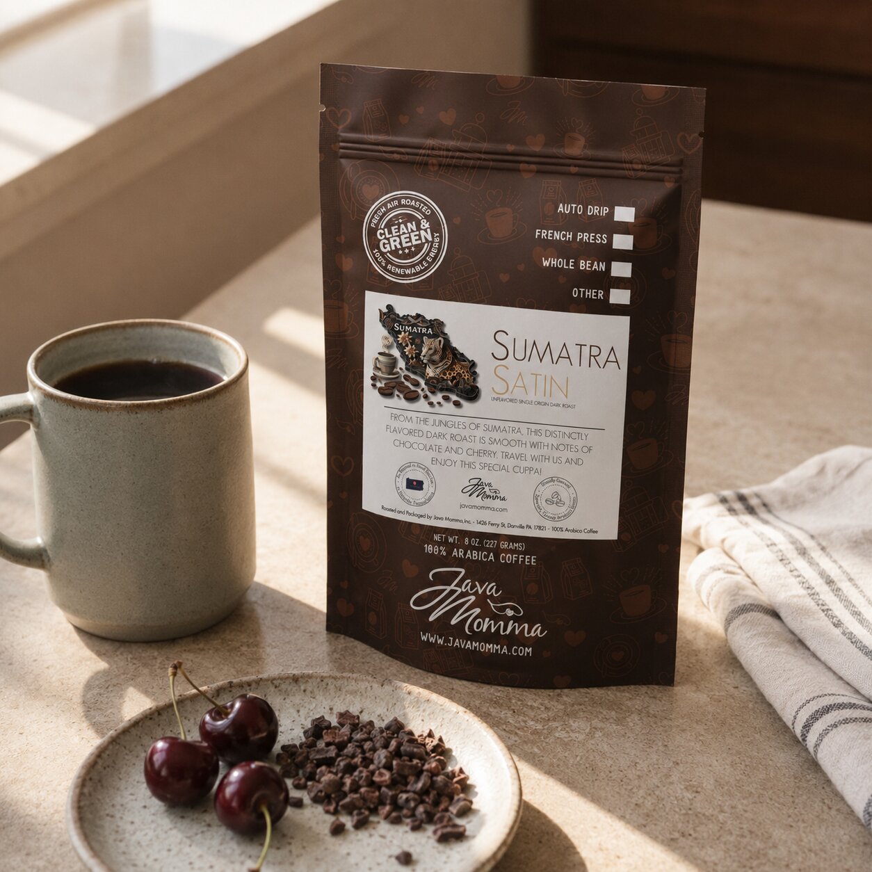 Java Momma Sumatra Satin Dark Roast coffee bag next to a mug of coffee with a few dark cherries and cacao nibs