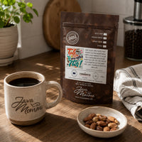 Thumbnail for Java Momma Talk to Me After This coffee bag next to a mug of coffee with a small dish of toasted almonds