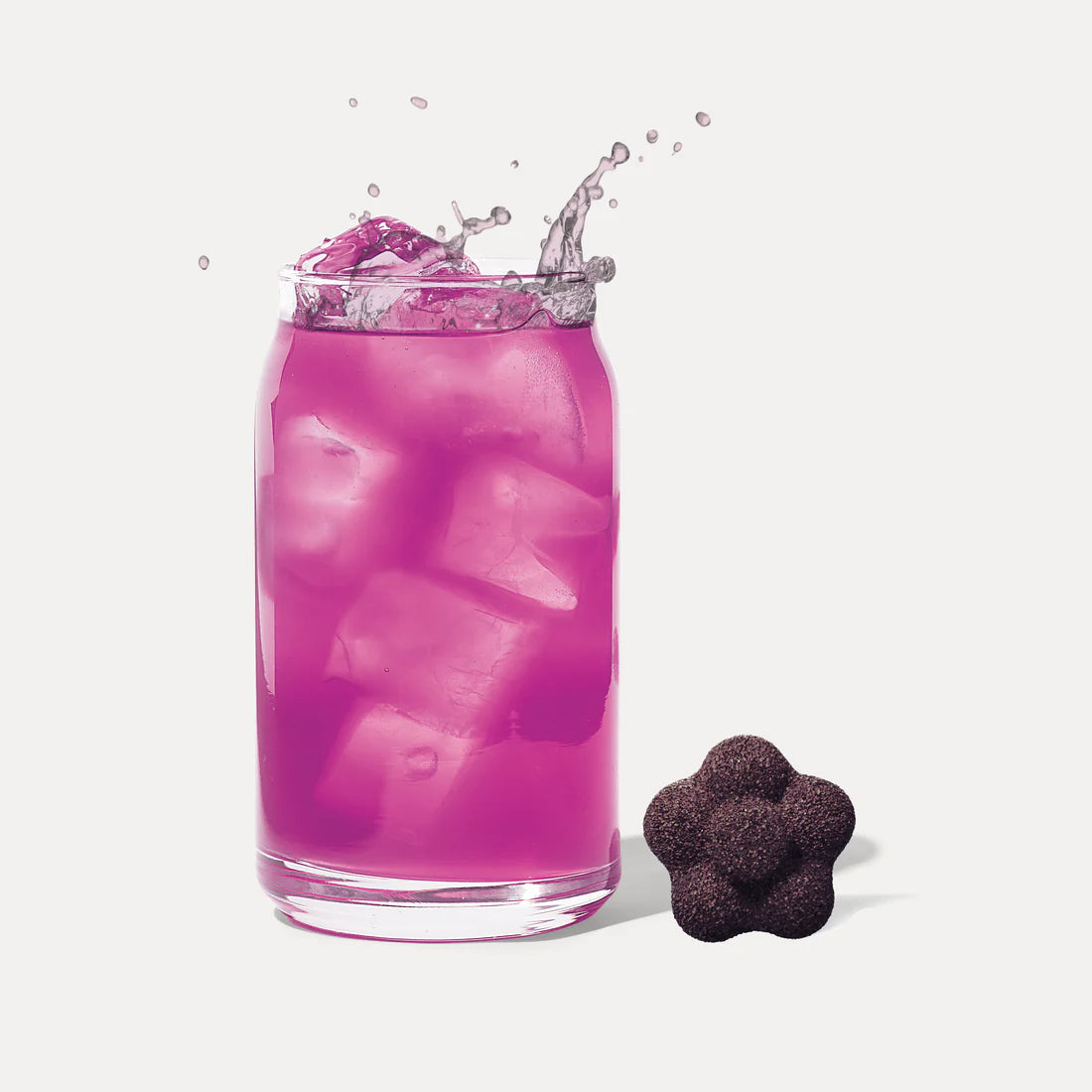 A glass of vibrant Ube Berries Tea Drop – Juicy, Antioxidant-Packed Purple Power 💜🍓🍒 with a splash effect, paired with a dark flower-shaped gummy on white background—a delicious, caffeine-free treat.