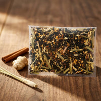 Thumbnail for Thai Chai Cold Brew Tea bag with dry herbs on a wooden surface with cinnamon, ginger, and a stick of cinnamon.