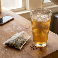 Thumbnail for Thai Chai cold brewed Iced tea being poured into a glass on a wooden table with a tea bag and smartphone in the background.