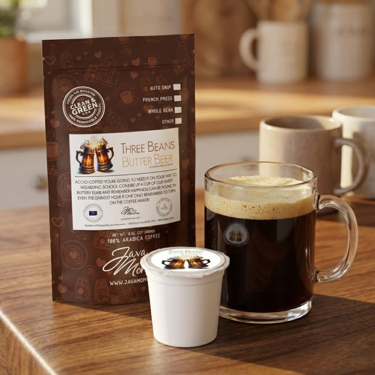 Three Beans Butter Beer coffee bag with single serve pod and glass mug of freshly brewed coffee with light foam on a warm wood kitchen counter.