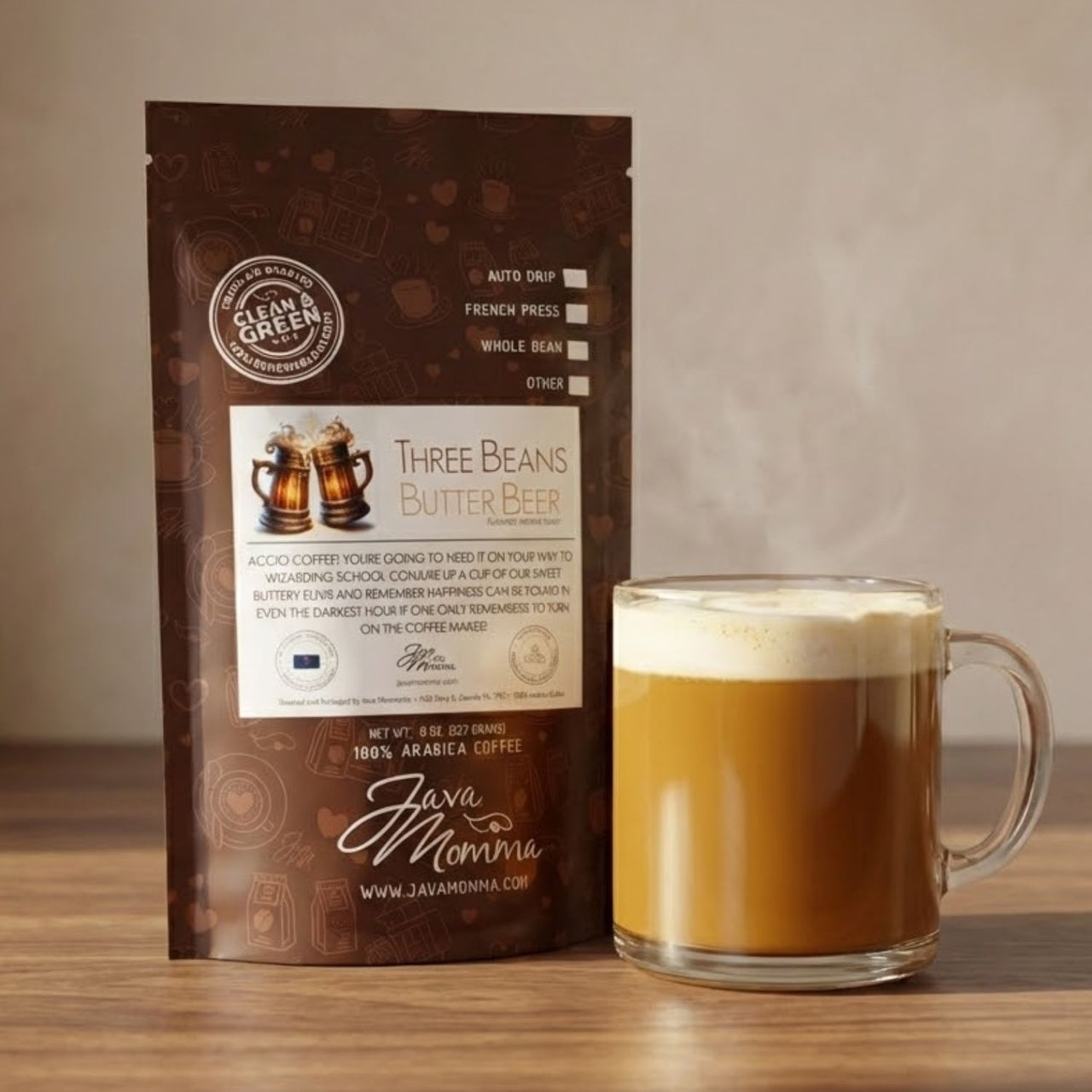 Three Beans Butter Beer flavored medium roast coffee bag in envelope-style packaging next to a clear glass mug of freshly brewed coffee with light foam.