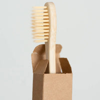 Thumbnail for The Bamboo Toothbrush – Eco-Friendly, Biodegradable Handle & Medium Bristles stands upright, partially visible in an open brown cardboard box against a plain light background.