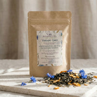 Thumbnail for Tea package labeled 'Verdant Grey' with tea leaves and flowers on a stone surface.
