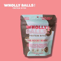 Thumbnail for A pink and brown pack of The Rocky Roadie – Chocolate Almond White Chip Wholly Balls sits on a pink background. This plant-based protein snack is gluten-free, dairy-free, contains 3g protein, almonds, white chips, and peanuts.